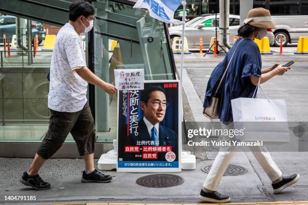 People walk past a campaign poster featuring a picture of Japanese Prime Minister Fumio Kishida during a Liberal Democratic Party campaign rally on...