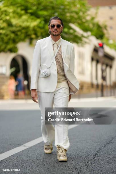 Guest wears beige sunglasses, a white latte cut-out pattern short sleeves polo shirt, a white latte blazer jacket, a white shiny leather micro...