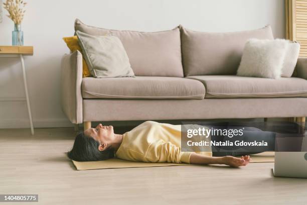 home fitness. elderly woman with closed eyes resting after workout. calm peaceful senior woman practicing shavasana or corpse pose in morning while lying on yoga mat on floor in living room at home, full length. - savasana stock pictures, royalty-free photos & images