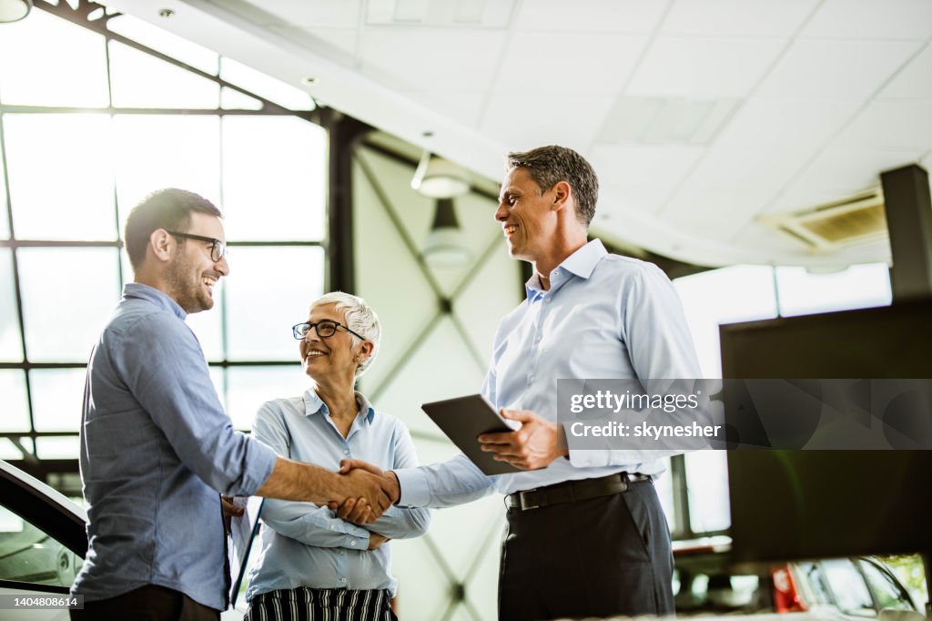 Business colleagues came to an agreement with car salesperson in a showroom.