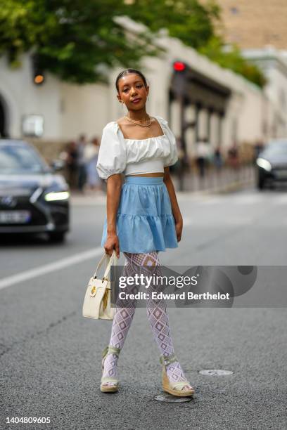 Guest wears gold earrings, gold chain necklaces, a gold headband, a white square-neck / puffy short sleeves cropped top, high waist blue denim short...