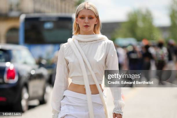 Guest wears a silver piercing, a white fluffy long scarf, a white latte ruffled long sleeves cropped t-shirt, high waist white wrap knees skirt,...