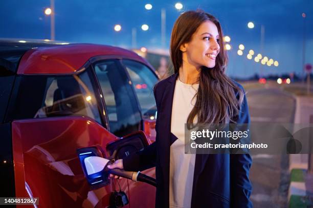 portrait of young woman charging her electric car - battery life stock pictures, royalty-free photos & images