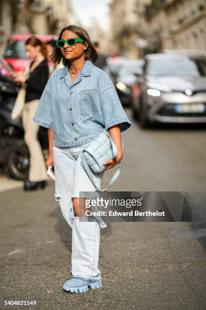 Guest wears green sunglasses from Miu Miu, a silver chain necklace, a blue denim short sleeves oversized shirt, a pale blue shiny leather Cassette...