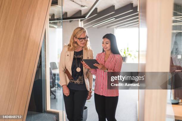multiracial mixed age range female coworkers walking with a digital tablet - assistente stockfoto's en -beelden