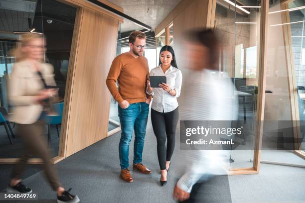 caucasian male and asian female coworkers using a digital tablet at the office - blurred motion people walking stock pictures, royalty-free photos & images