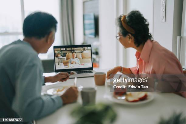looking over shoulder asian chinese senior couple videocall granddaughter using laptop in dining room during weekend morning  breakfast leisure time - silver surfer stock pictures, royalty-free photos & images