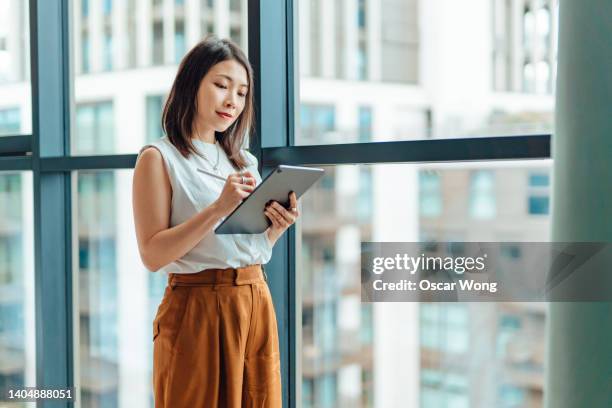young business woman using digital tablet, standing next to the window in the office - vestuário de trabalho imagens e fotografias de stock