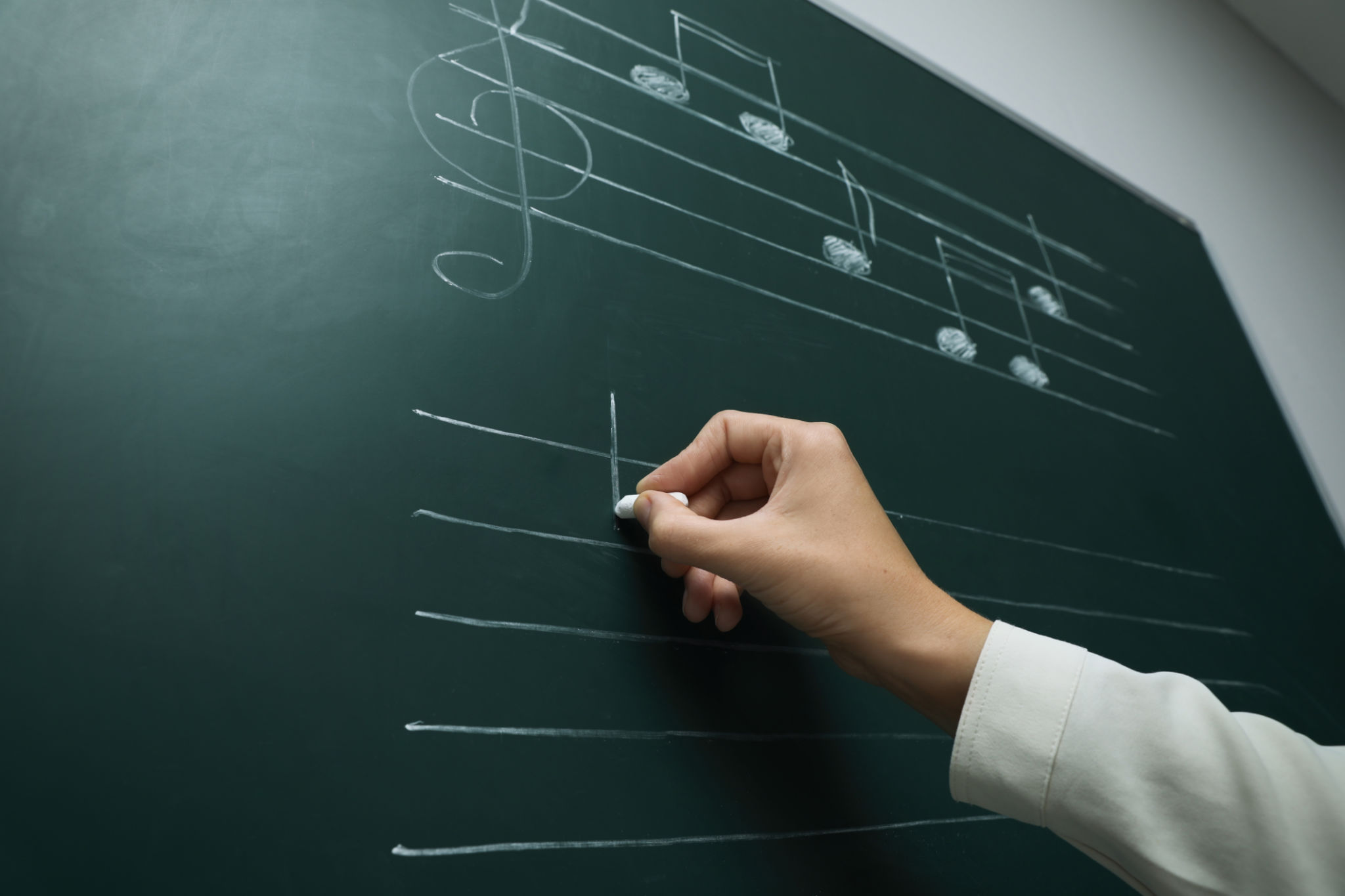 Teacher writing music notes with chalk on greenboard, closeup Teacher writing music notes with chalk on greenboard, closeup