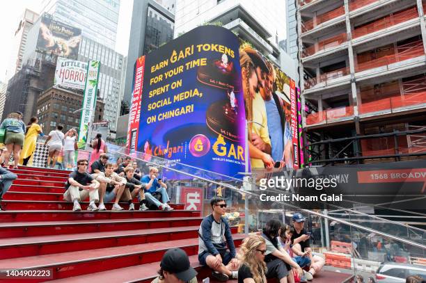 People sit by a Chingari and Gari Token billboard in Times Square during the 4th annual NFT.NYC conference on June 23, 2022 in New York City. The...
