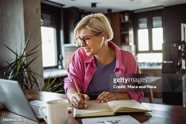 cheerful young woman taking notes and working at home - computer learning stockfoto's en -beelden