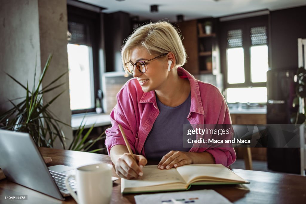 Cheerful young woman taking notes and working at home