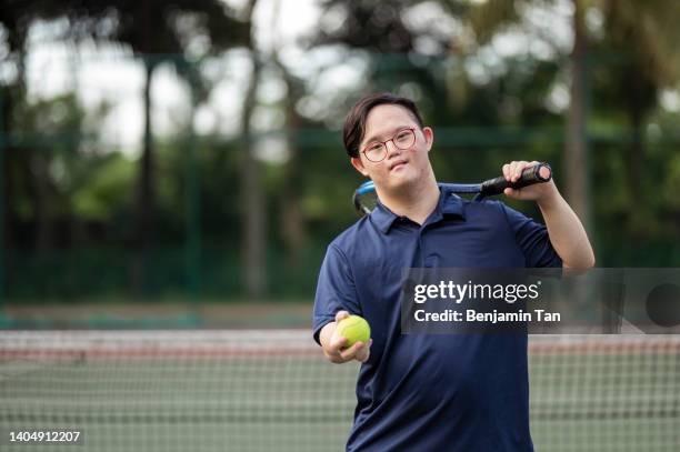 portrait asian chinese down syndrome male tennis player looking at camera at tennis court - tennis adult stock pictures, royalty-free photos & images