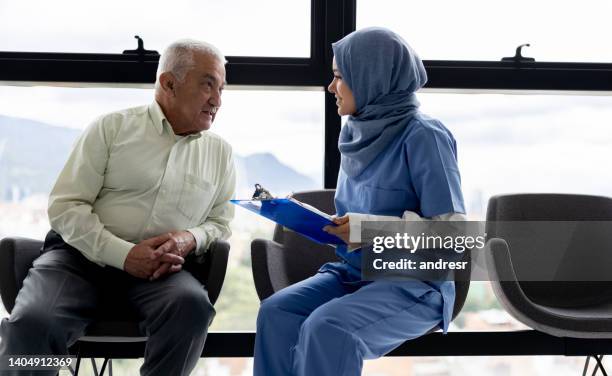 muslim female doctor talking to a senior man at the hospital - arabic doctor stockfoto's en -beelden