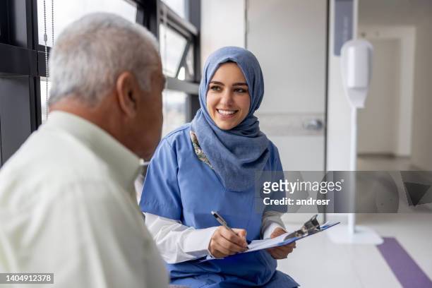 muslimische krankenschwester, die mit einem älteren patienten im krankenhaus spricht - headgear stock-fotos und bilder