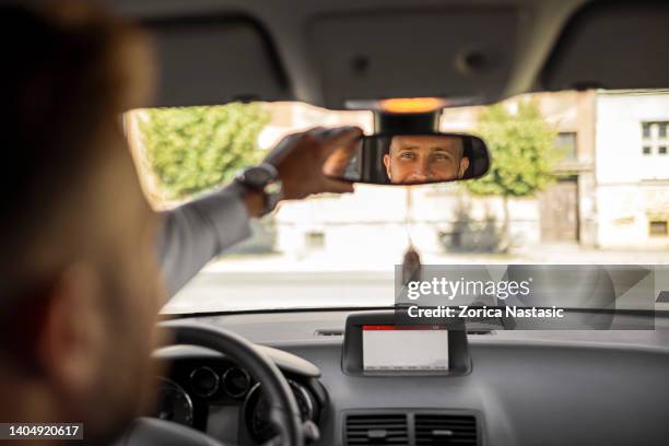 uomo d'affari serio che guida un'auto guardando lo specchietto retrovisore - specchietto di veicolo foto e immagini stock