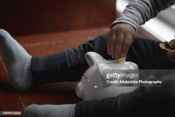 toddler putting gold coin in piggy bank - save our future babies stock pictures, royalty-free photos & images