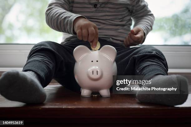 toddler putting gold coin in piggy bank - save our future babies stock pictures, royalty-free photos & images