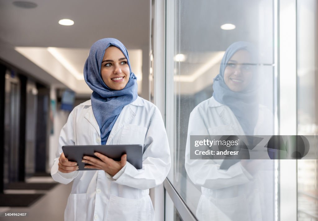 Glücklicher muslimischer Arzt, der im Krankenhaus mit einem Tablet arbeitet