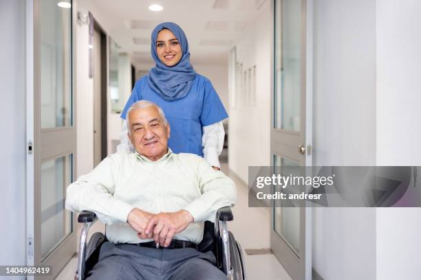 muslimische krankenschwester, die sich um einen älteren mann im rollstuhl kümmert - arab doctor patient stock-fotos und bilder