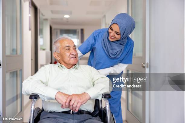 infermiera musulmana che si prende cura di un paziente anziano su una sedia a rotelle - doctor supporting patient foto e immagini stock