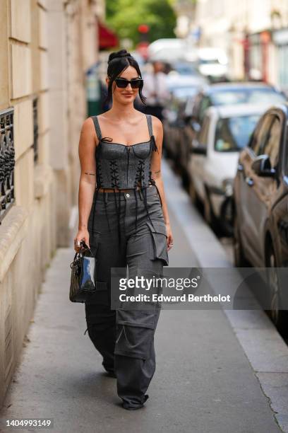 Fiona Zanetti wears black sunglasses, a gray laces / square neck / corset tank-top, high waist dark gray large cargo pants, a black shiny varnished...
