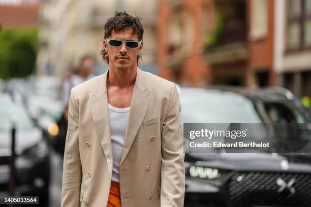 Guest wears green sunglasses, a beige long blazer jacket, a white tank-top, orange shorts, outside the Dior Homme show, during Paris Fashion Week -...