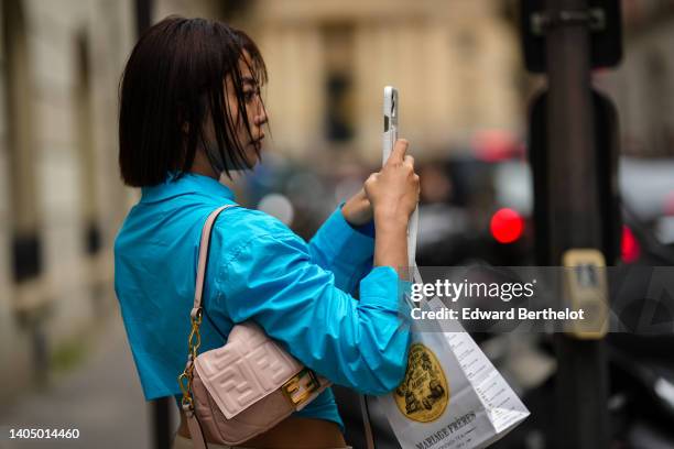 Guest wears a blue cropped shirt, a white shopping bag from Mariage Freres, a pale pink FF monogram embossed leather shoulder bag, outside the Dior...