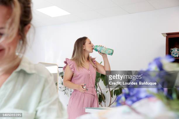 woman holding reusable stainless steel water bottle at work - reusable water bottle office stock pictures, royalty-free photos & images