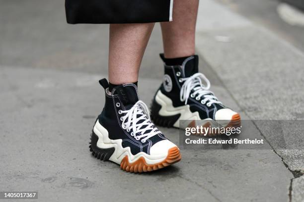 Guest wears a black with white borders long coat, black laces ankle sneakers, outside the Comme des Garçons Homme Plus show, during Paris Fashion...