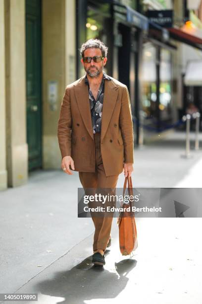 Guest wears khaki sunglasses, a black with silver print pattern shirt, a brown blazer jacket, brown suit pants, a silver rings, a brown shiny leather...