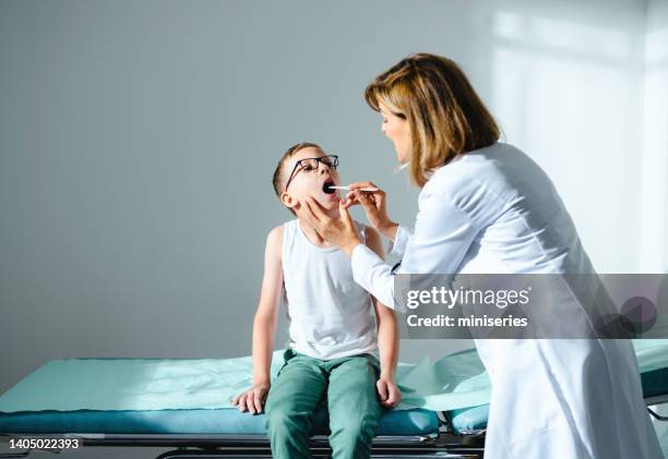 weibliche kinderärztin, die halsschmerzen eines jungen untersucht - kehle stock-fotos und bilder
