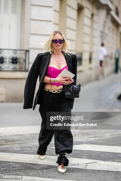 Guest wears futurist sunglasses, silver earrings, a black oversized blazer jacket, a neon pink shoulder-off / cropped top, a gold chain belt, black...