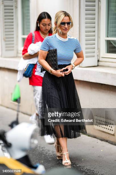 Guest wears black sunglasses, a white and blue striped print pattern t-shirt, a black shiny leather quilted pattern clutch from Dior, a black polka...