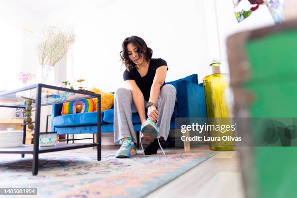 young adult woman sits on her sofa and puts on her shoes - women trying on shoes 個照片及圖片檔