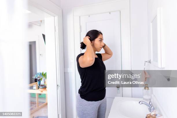 young adult woman checks her hair in the bathroom mirror - combing foto e immagini stock