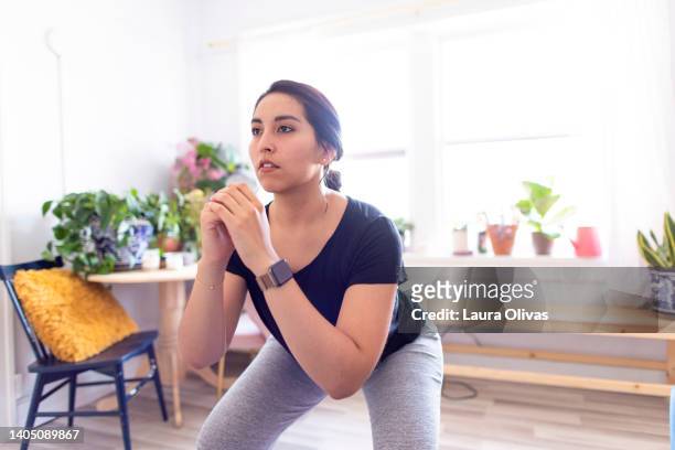 young adult woman exercising in her apartment - squatting position - fotografias e filmes do acervo