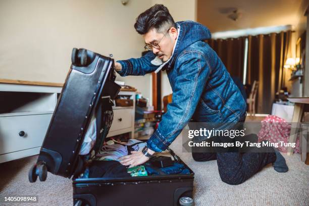 young asian man packing a suitcase for trip at home - packing travel stock-fotos und bilder