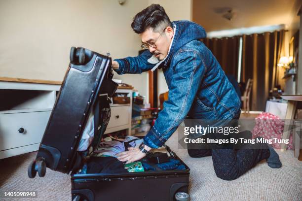 young asian man packing a suitcase for trip at home - suitcase packing stockfoto's en -beelden