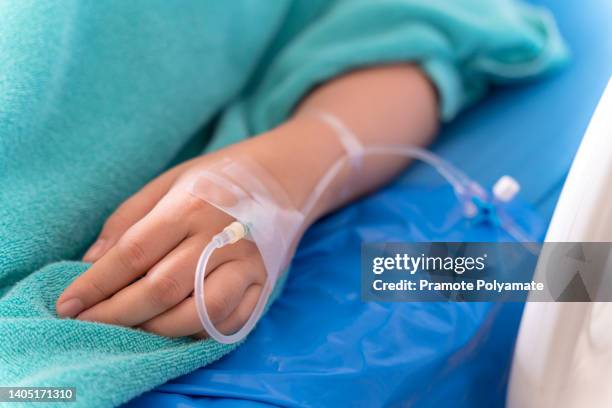 hand of the patient is on drip receiving a saline solution on bed vip room at hospital. medical concept. - infused - fotografias e filmes do acervo