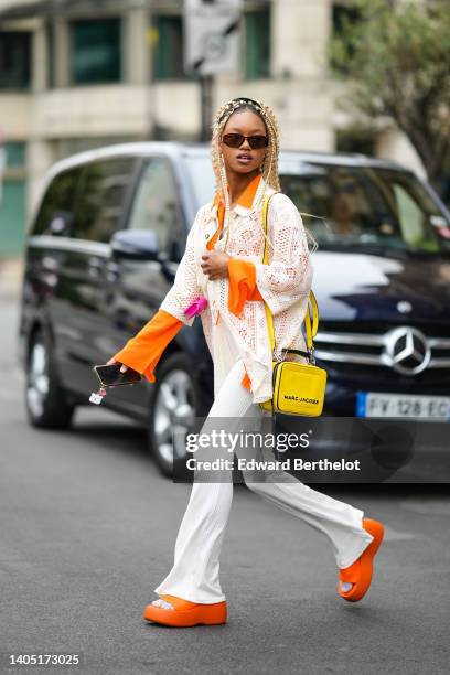 Debbie @blackhey wears brown with orange details sunglasses, an orange shirt, a white cut-out pattern oversized short sleeves shirt, a neon pink...