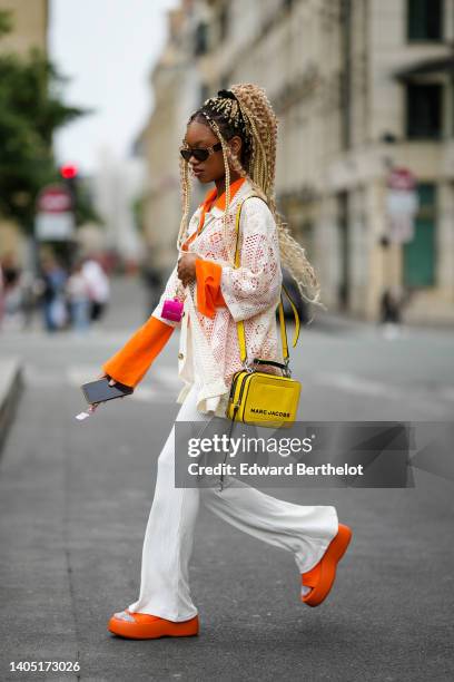 Debbie @blackhey wears brown with orange details sunglasses, an orange shirt, a white cut-out pattern oversized short sleeves shirt, a neon pink...