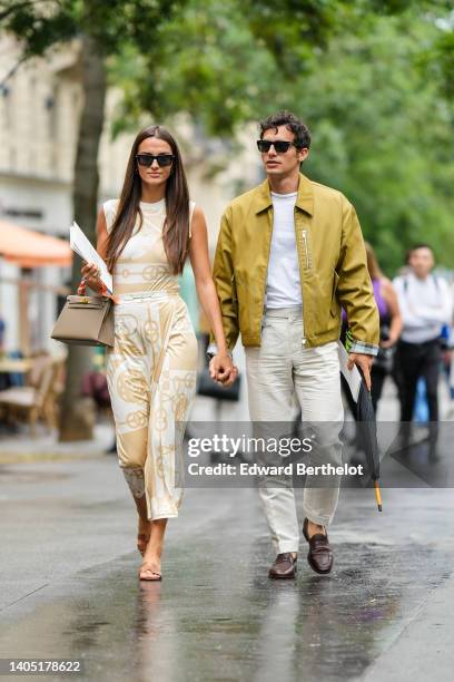 Gabrielle Caunesil wears black sunglasses, silver earrings, a white latte and beige print pattern sleeveless tank-top from Hermes, matching beige and...