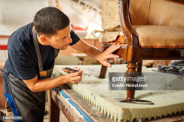 upholstery worker examining a chair on a workshop bench - restoring chair stock pictures, royalty-free photos & images