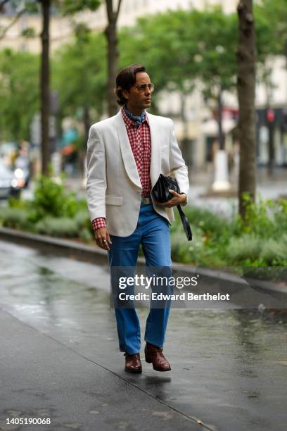 Guest wears aviator sunglasses, a blue print pattern scarf, a white and red checkered print pattern shirt, a white blazer jacket, a black shiny...