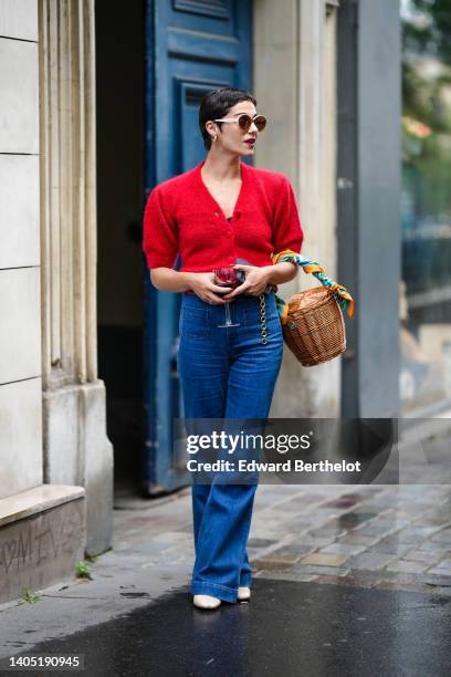 Guest wears circle sunglasses, a red fluffy puffy short sleeves / buttoned cropped cardigan, navy blue denim wide legs pants, a brown wickers basket...