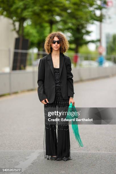 Guest wears black sunglasses, a black satin with embroidered fishnet with silver pearls and fringed details V-neck / jumpsuit, a black blazer jacket,...