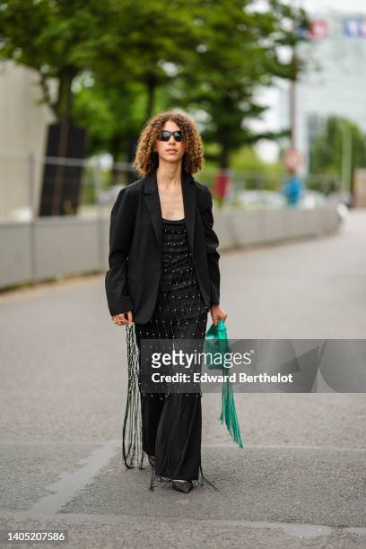 Guest wears black sunglasses, a black satin with embroidered fishnet with silver pearls and fringed details V-neck / jumpsuit, a black blazer jacket,...