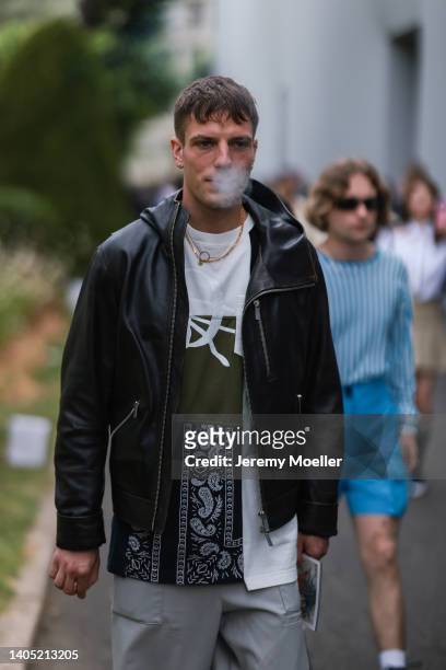 Guest seen wearing a black hooded leather jacket, gold necklace, a white/khaki/black pattern t-shirt and a grey nylon cargo pants, outside the Dior...