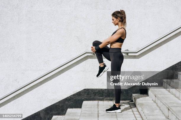 beautiful female athlete doing warm-up before jogging outdoors against the background of a white wall on a city street. copy space. sports concept. full length. - cardio ストックフォトと画像